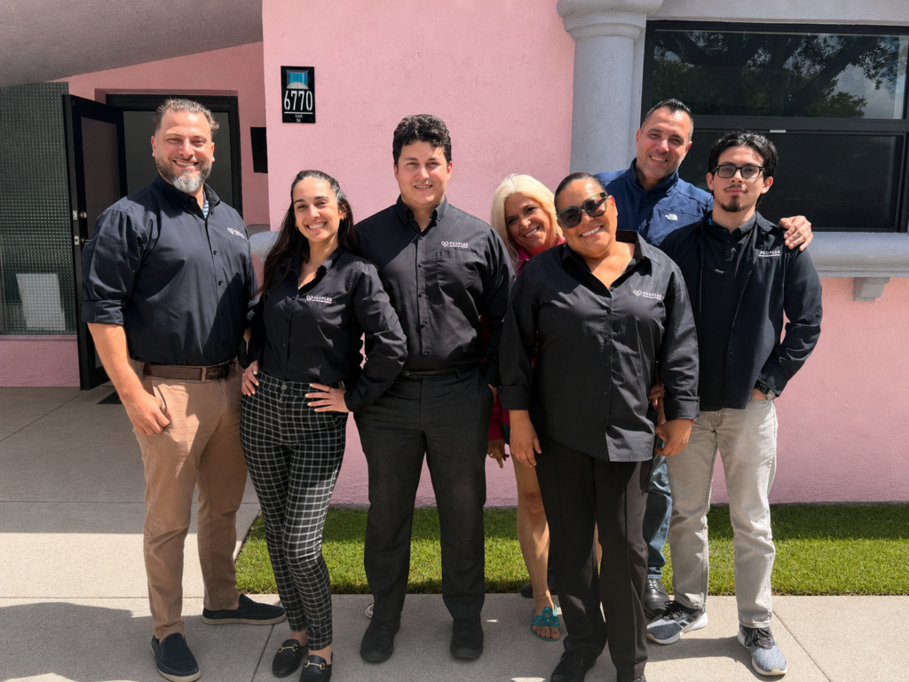 A group of friendly insurance agents pose for a team photo outside of their office.